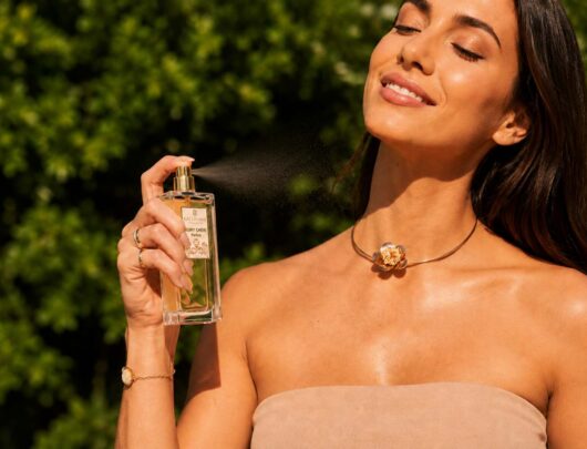 Parfum Ruby Chéri vaporisé par une femme souriante en extérieur, fragrance féminine raffinée aux notes gourmandes et florales.