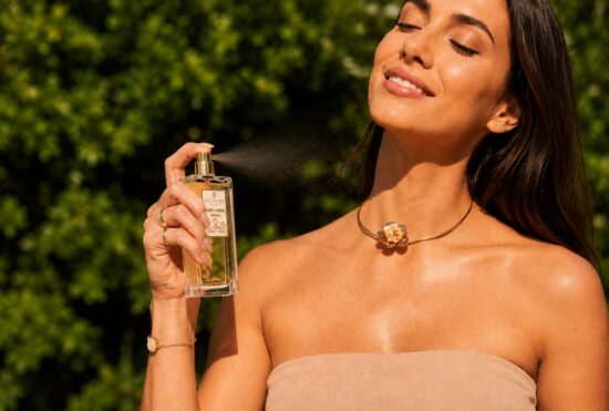 Parfum Ruby Chéri vaporisé par une femme souriante en extérieur, fragrance féminine raffinée aux notes gourmandes et florales.